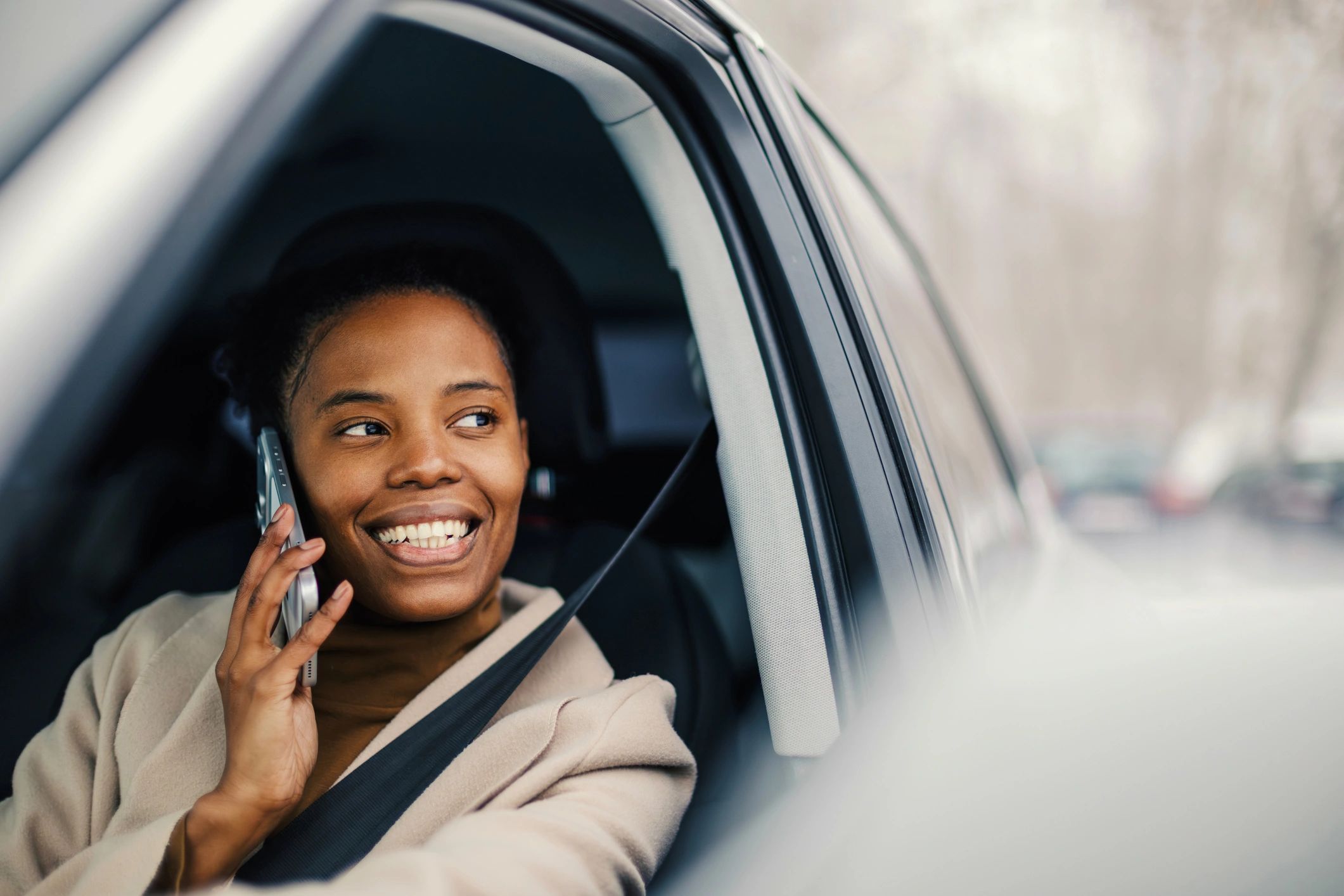 Woman smiling while talking on a phone in a car